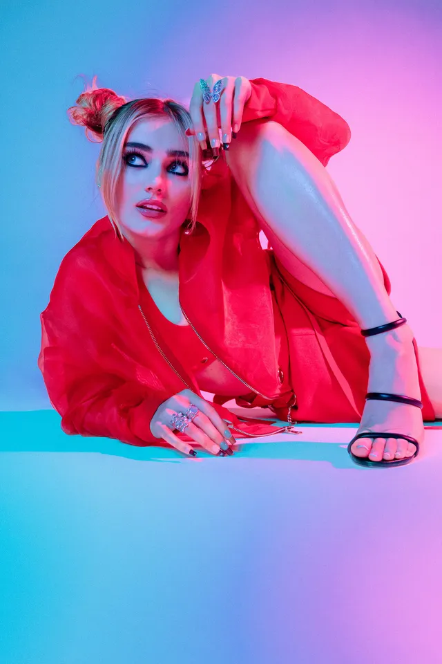 Meg Donnelly crouching in a red outfit and black heels for a studio portrait.