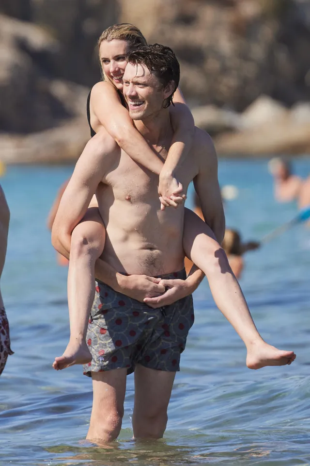 Emma Roberts riding on a companion in shallow water with bare feet visible.