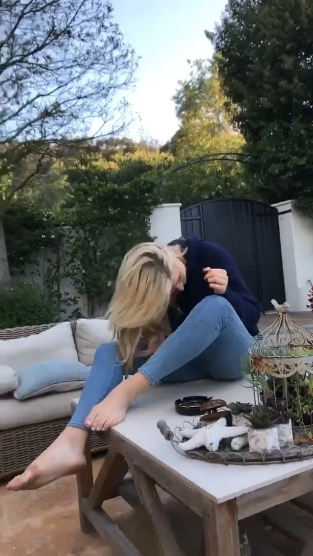 Chloë Grace Moretz sitting barefoot beside an outdoor table.