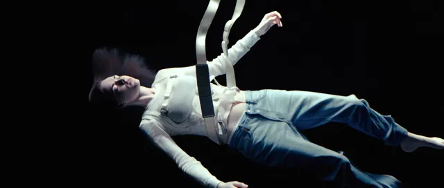 Cara Delevingne appearing suspended in a dark screen scene.