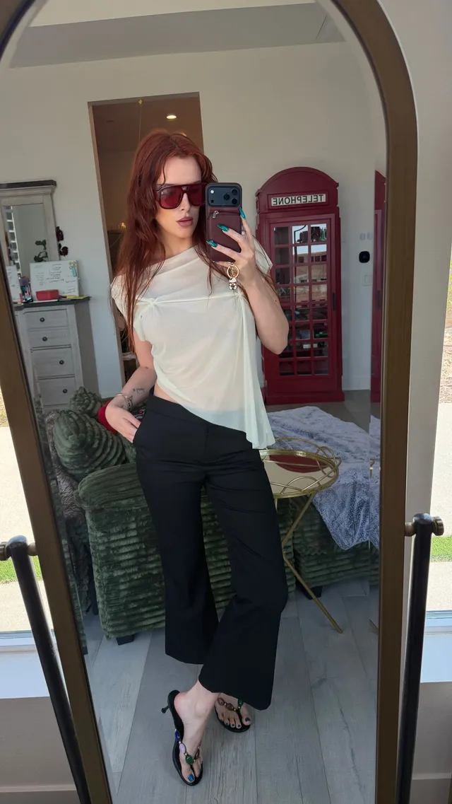 Bella Thorne posing in dark trousers and heels for a mirror photo.