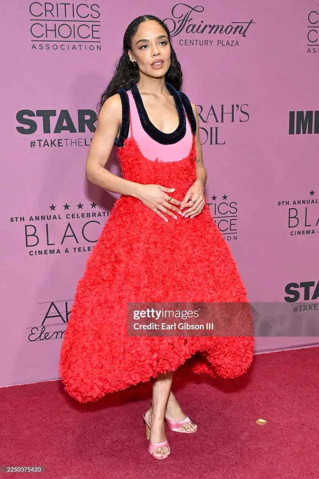 Tessa Thompson posing in a textured red dress at an event.