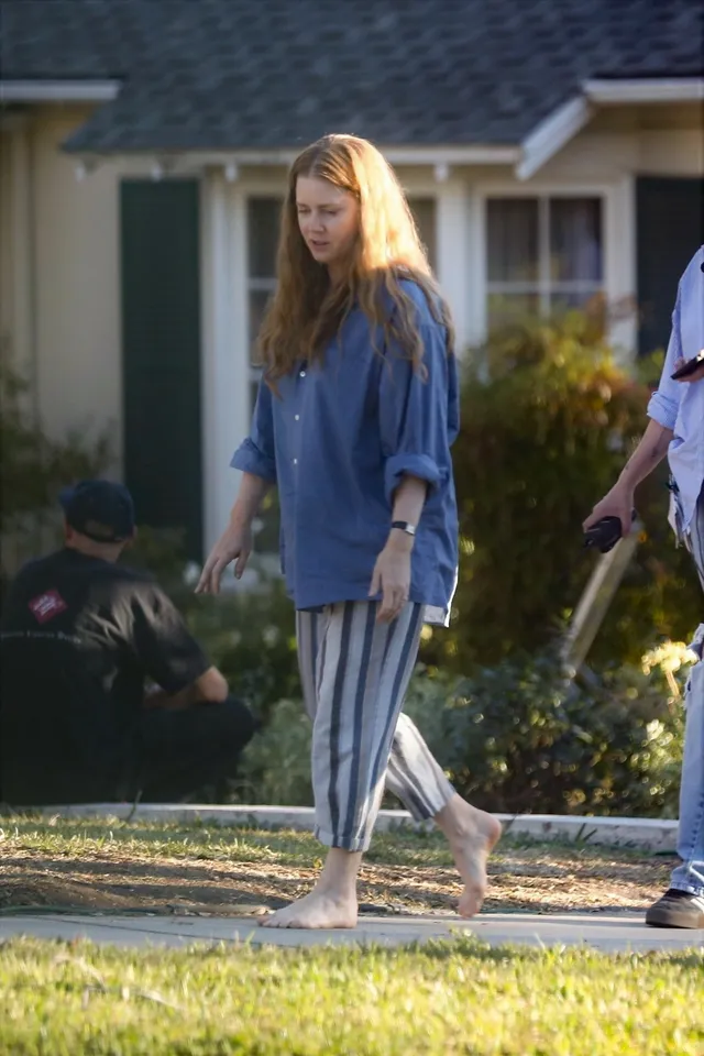 Amy Adams walking across grass in a loose casual outfit.