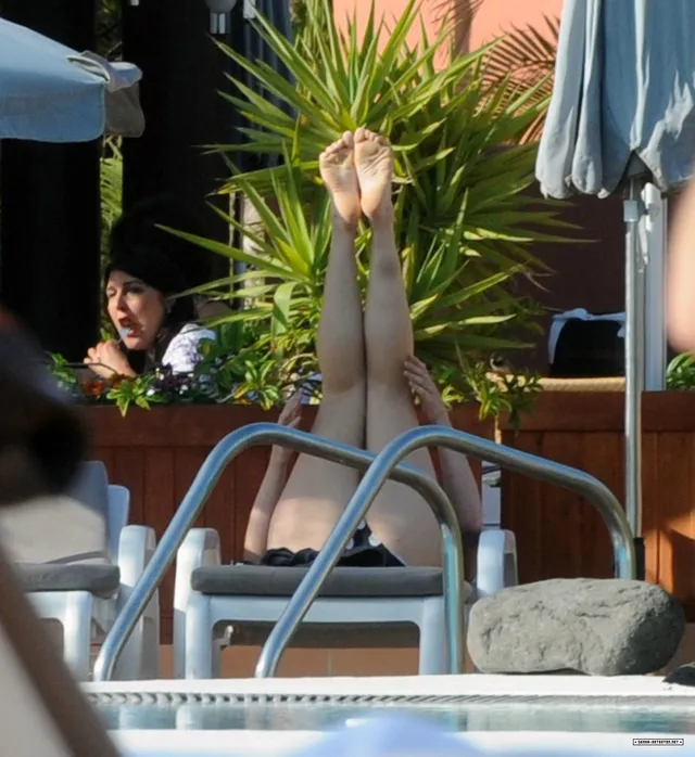 Gemma Arterton relaxing beside a pool with her feet raised.