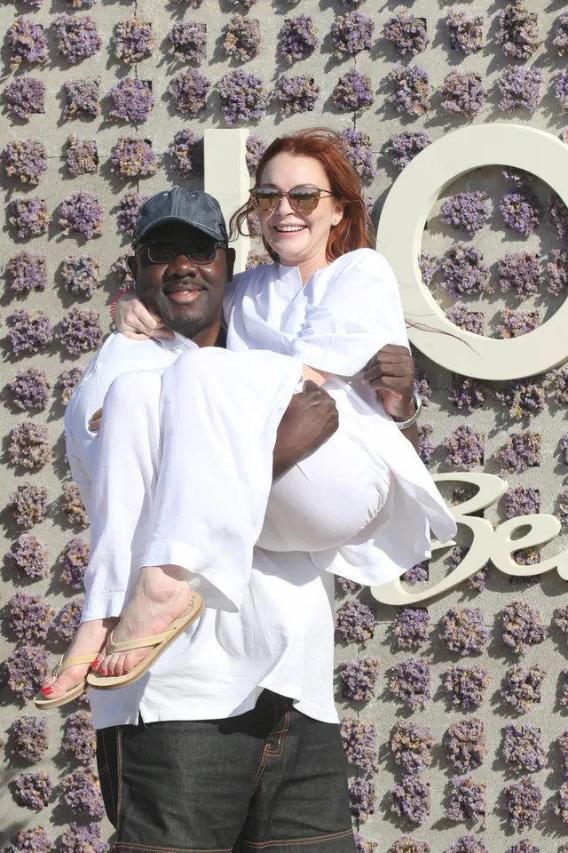 Lindsay Lohan wearing white and sandals while a man holds her at an event.