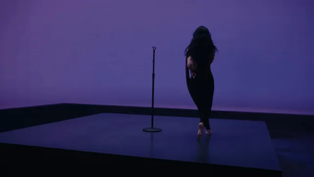 Demi Lovato walking barefoot beside a microphone in a purple-lit studio setting.