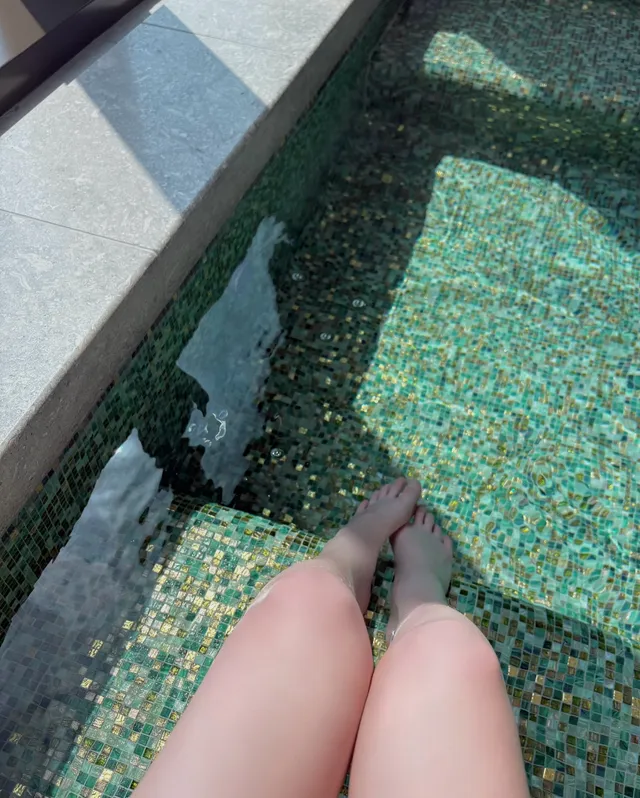 Jang Wonyoung resting bare feet in shallow water.