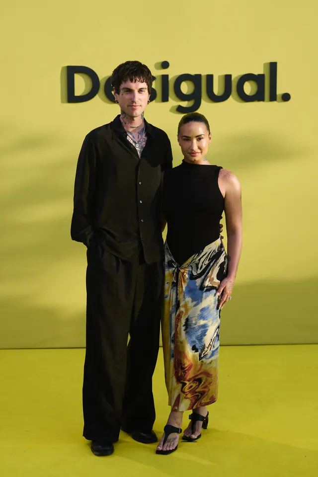 Demi Lovato standing beside another person in patterned trousers and heels.