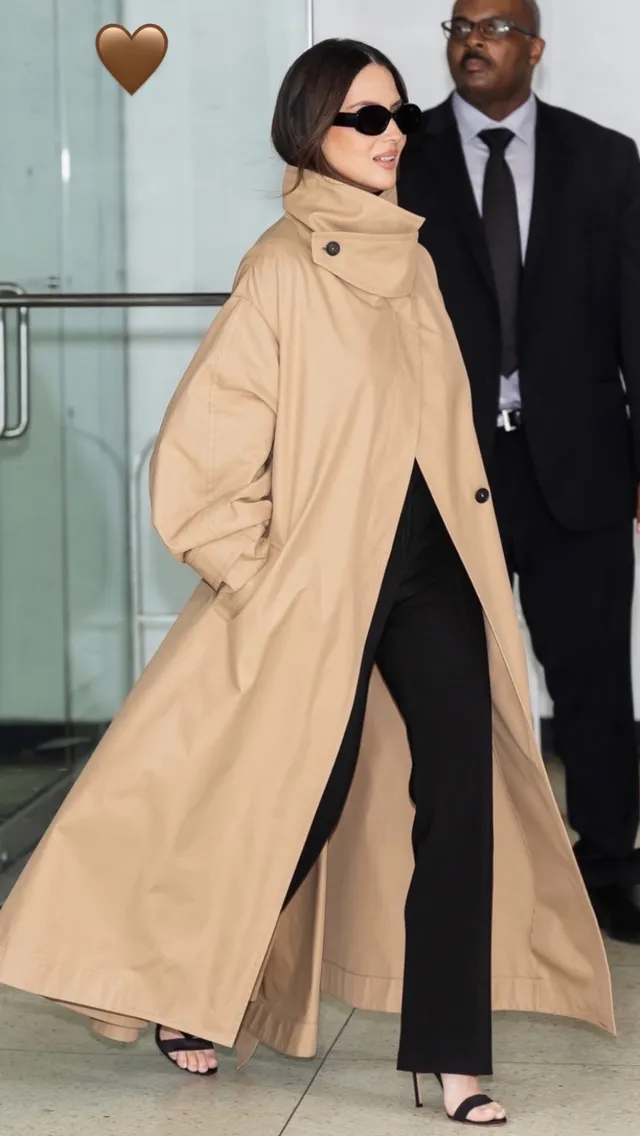 Olivia Munn walking outdoors in a beige coat and black heels.