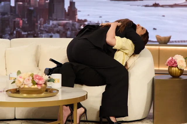 Olivia Munn leaning toward another person on a television sofa in black heels.