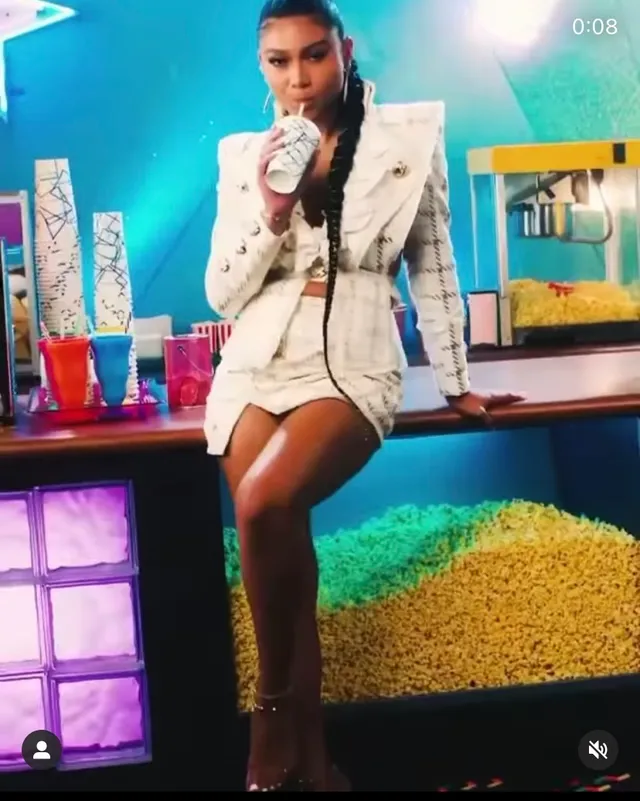 Sierra Capri sitting on a colorful set in a white outfit and heels.