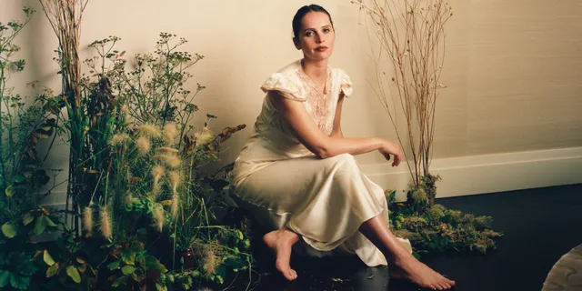 Felicity Jones sitting among plants in a pale dress.