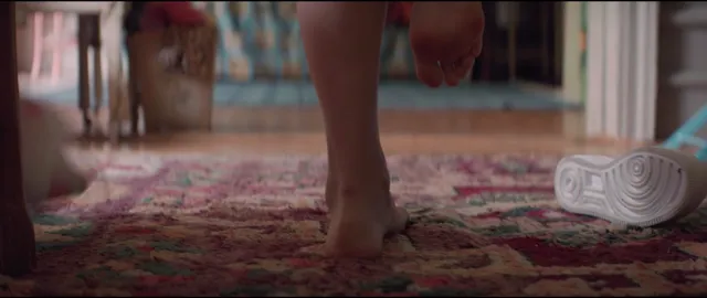 Melissa Barrera standing barefoot on a patterned rug in a film scene.