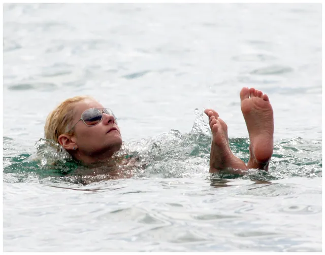 Elisha Cuthbert swimming with her bare soles raised above the water.