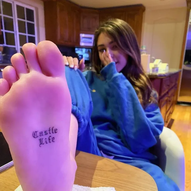 Madison Beer: holding a bare sole toward the camera indoors.