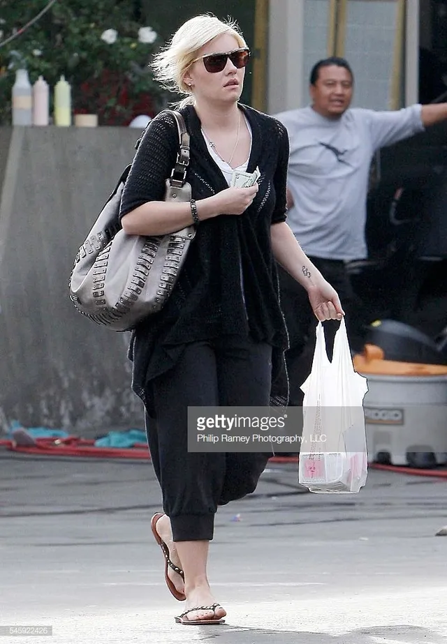 Elisha Cuthbert walking outdoors in cropped trousers and flip-flops.
