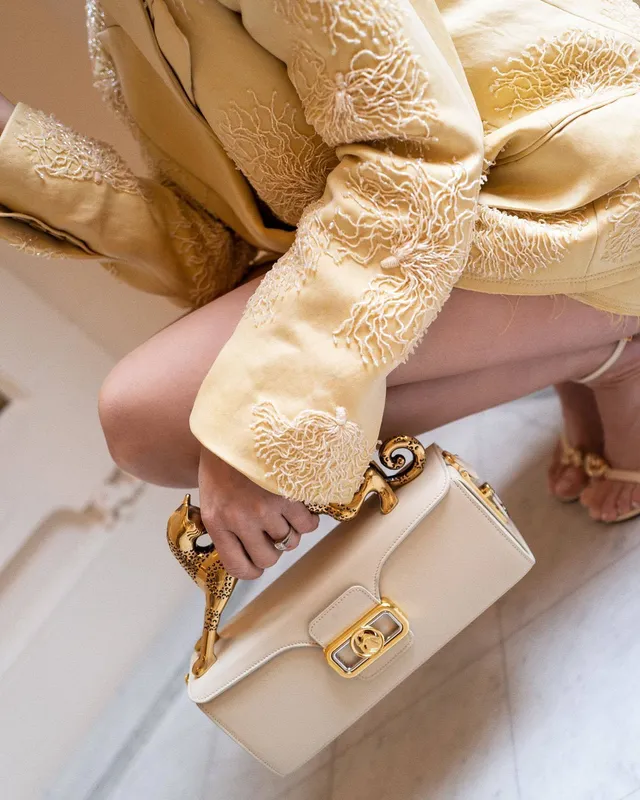 Josephine Skriver sitting barefoot in a yellow lace outfit with a handbag.