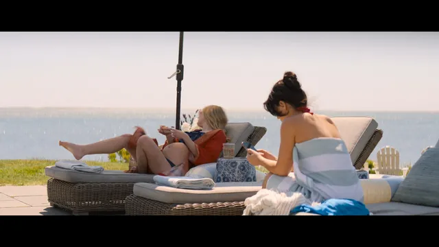Dakota Fanning relaxing barefoot on a lounger beside another woman.