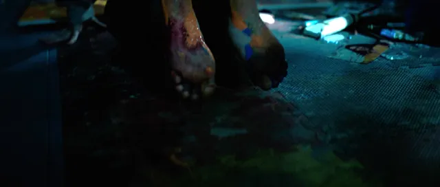 Sophie Thatcher with bare feet visible on a blue-lit floor in a film scene.