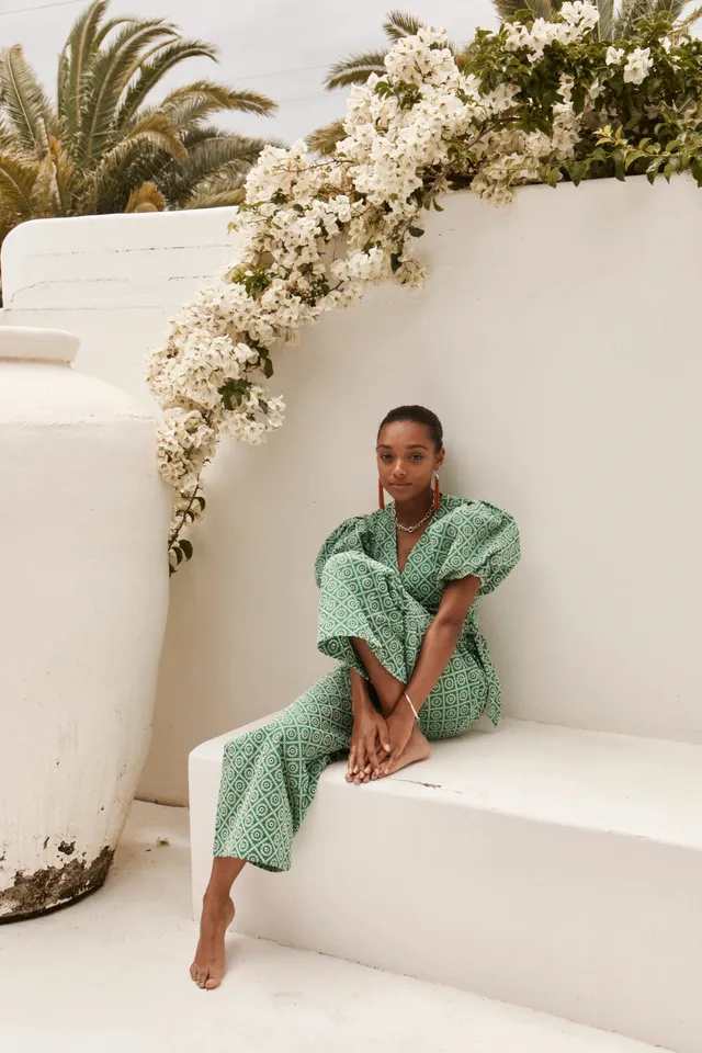 Sophie Wilde sitting barefoot on white steps in a green outfit.