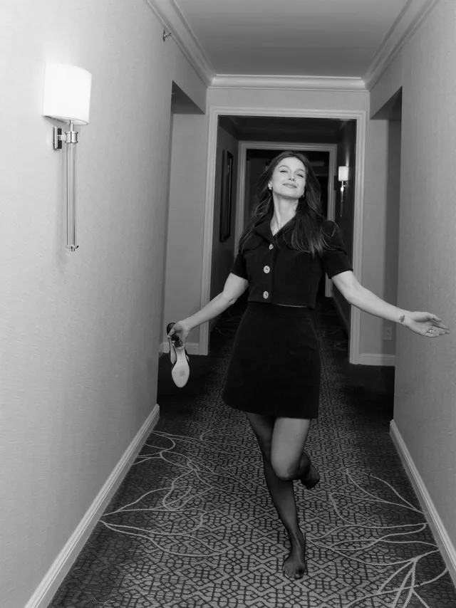 Melissa Benoist posing in a dark outfit and heels in a corridor.
