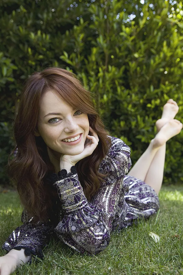 Emma Stone lying on grass with her bare feet lifted behind her.