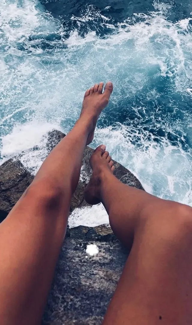 María Pedraza shown with bare legs extended beside breaking waves.