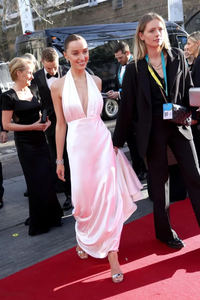 Phoebe Dynevor walking on a red carpet in a pink gown and silver heels.
