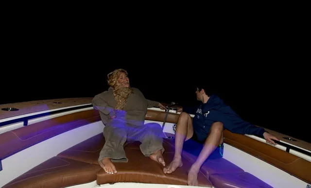 Iggy Azalea sitting barefoot on a boat beside another person at night.