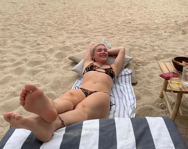Florence Pugh relaxing barefoot on a beach lounger with soles visible.