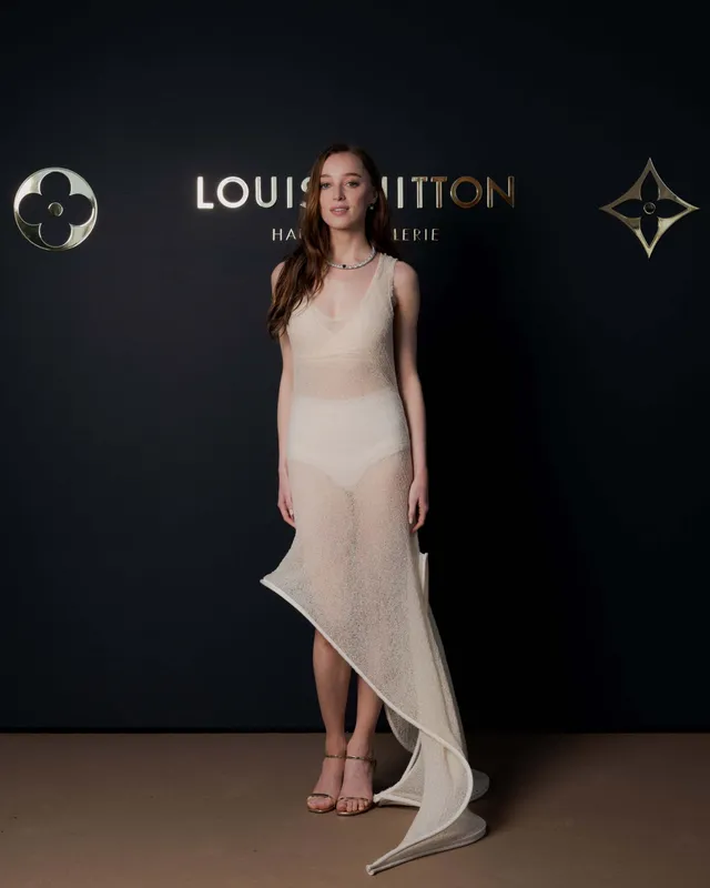 Phoebe Dynevor posing at a fashion event in a pale asymmetric dress.