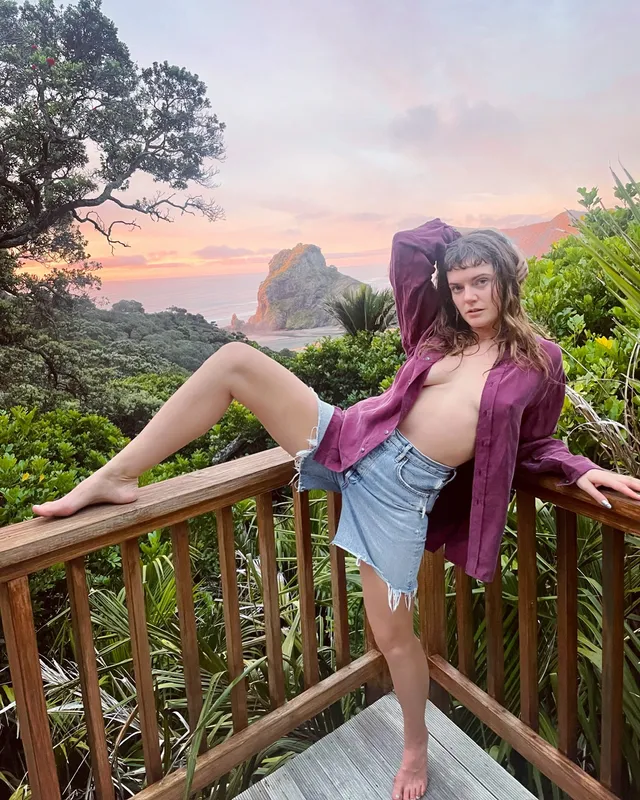 Tove Lo posing barefoot on a wooden balcony in denim shorts.