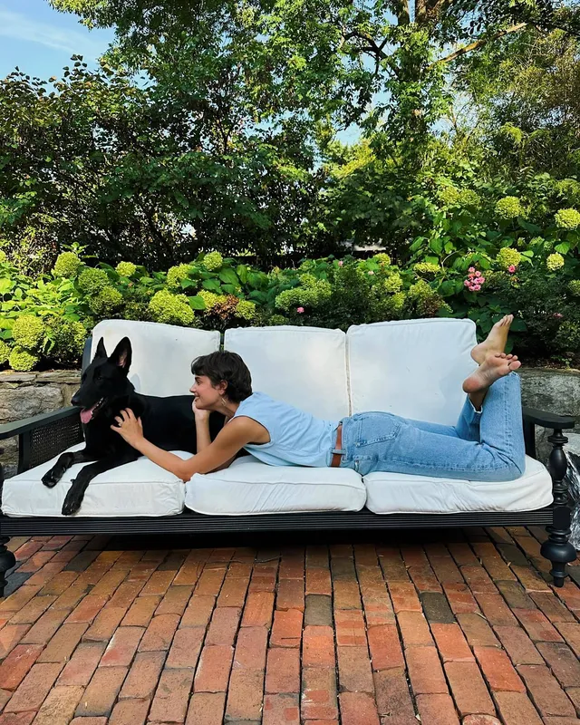 Taylor Hill lying on an outdoor sofa beside a dog with her bare feet raised.