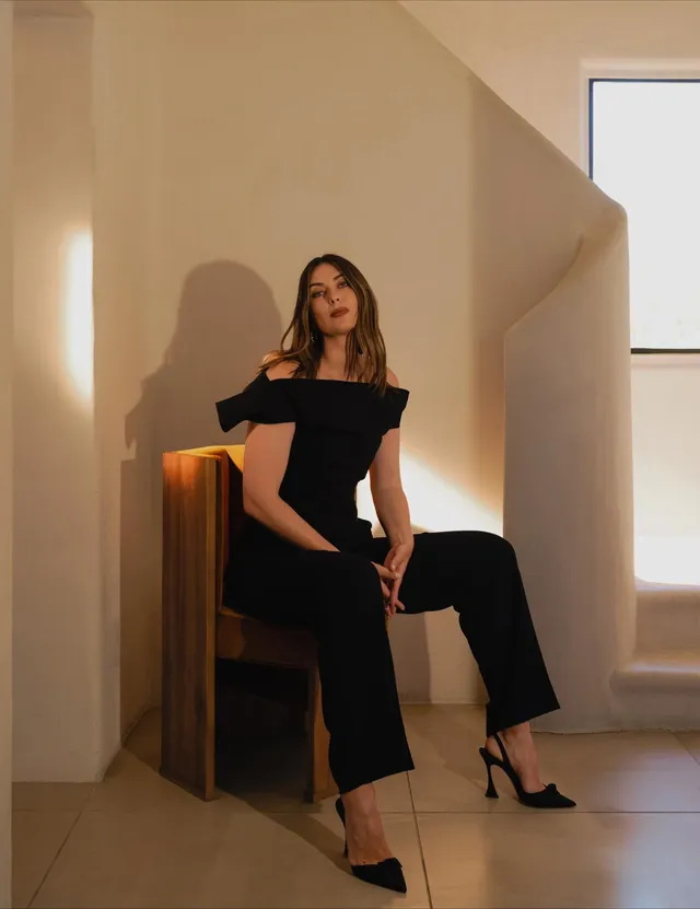 Maria Sharapova sitting in black pointed heels and a dark outfit in a sunlit room.