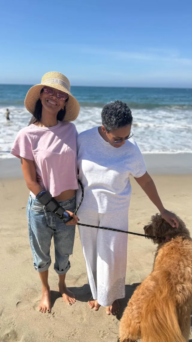 Zoe Saldaña standing on a beach with a companion and a dog.