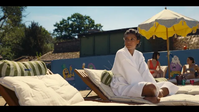 Sophie Wilde sitting barefoot on a sun lounger in a white robe.