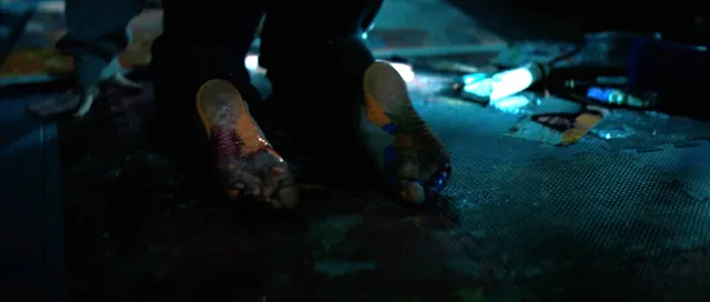 Sophie Thatcher with bare feet visible on a blue-lit floor in a film scene.