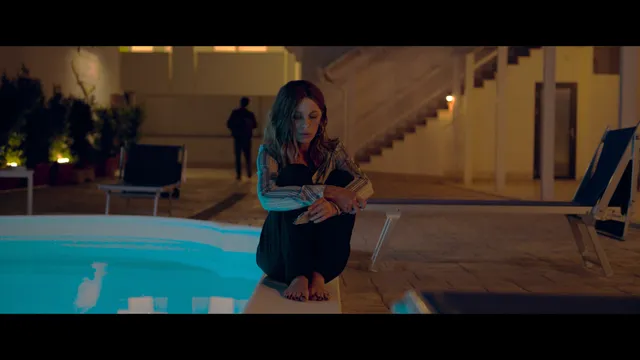 Kate Beckinsale sitting barefoot beside a swimming pool in a screen image.