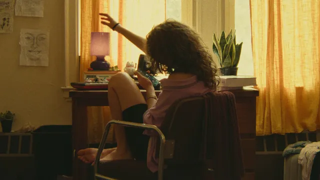 Odessa A'zion sitting barefoot on a chair in a scene.