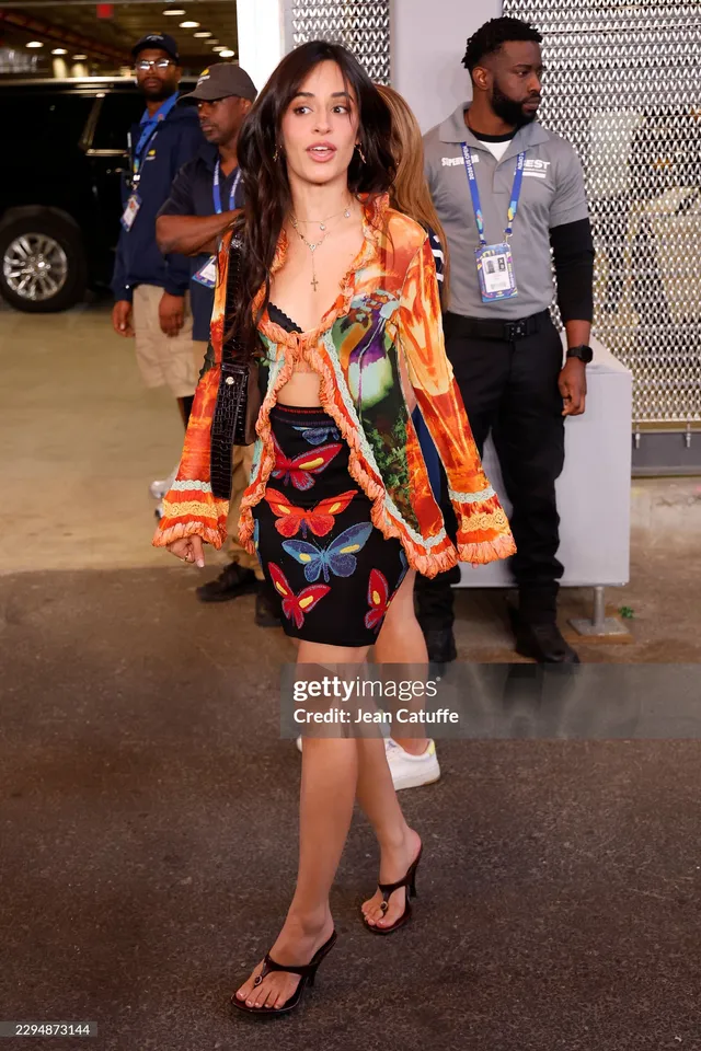 Camila Cabello standing in a colorful outfit and heels at an event.