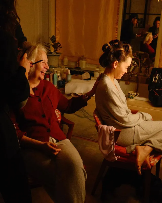 Emilia Clarke sitting at a table in a screen image with heels visible.