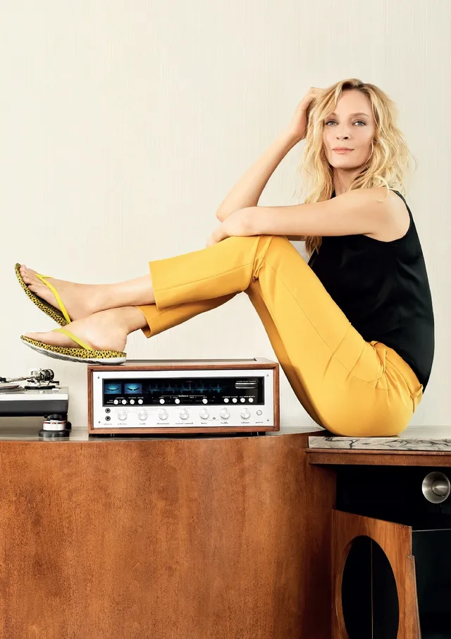 Uma Thurman sitting in yellow trousers and heels.