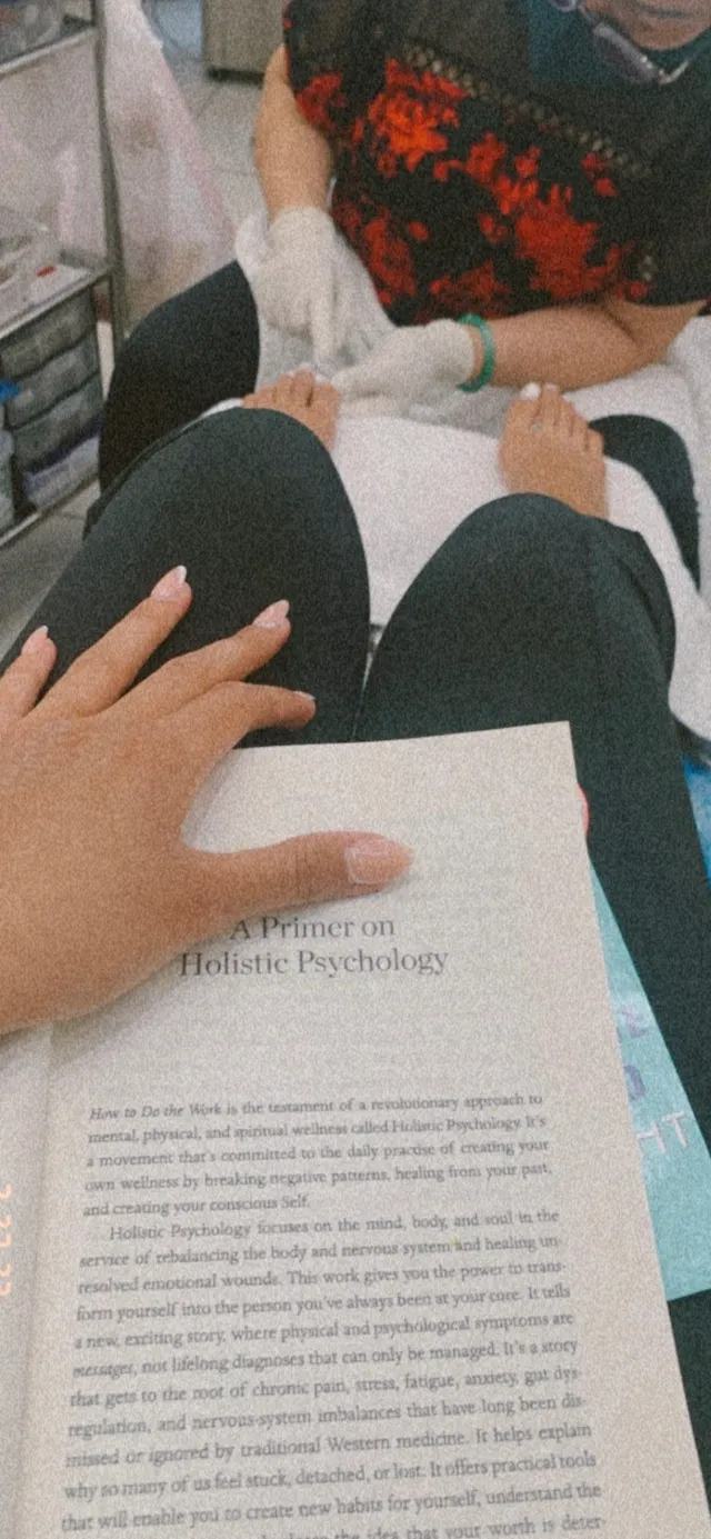 Emily Tosta reading a book with her bare feet resting ahead.