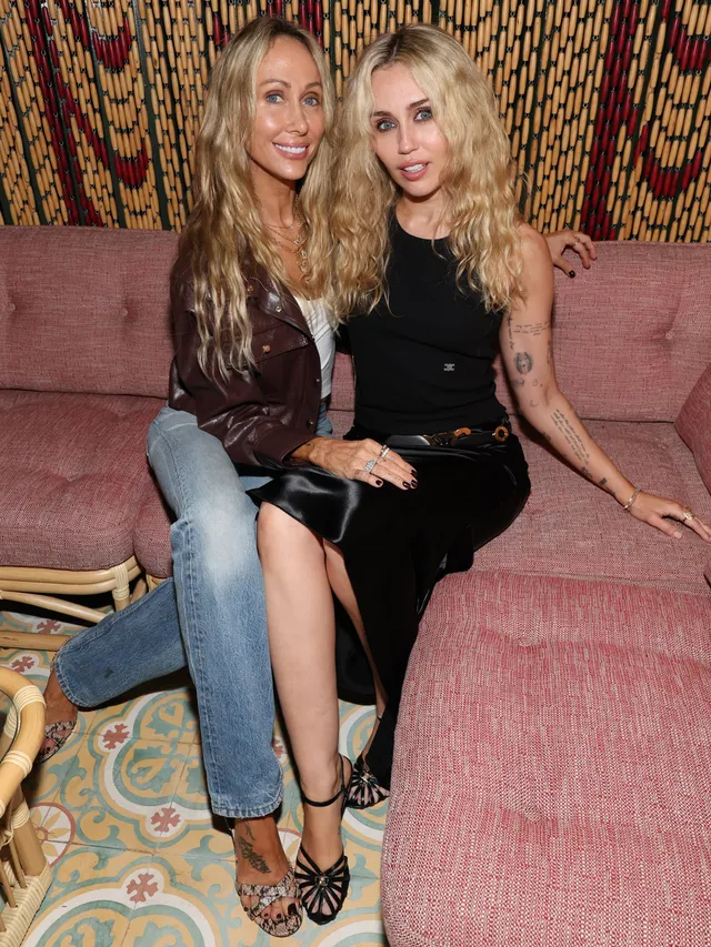 Miley Cyrus sitting with a friend on a sofa in black heels.