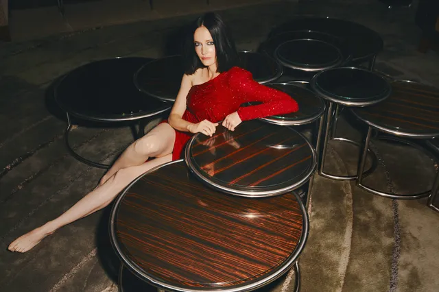 Eva Green seated among wooden tables in a red dress.