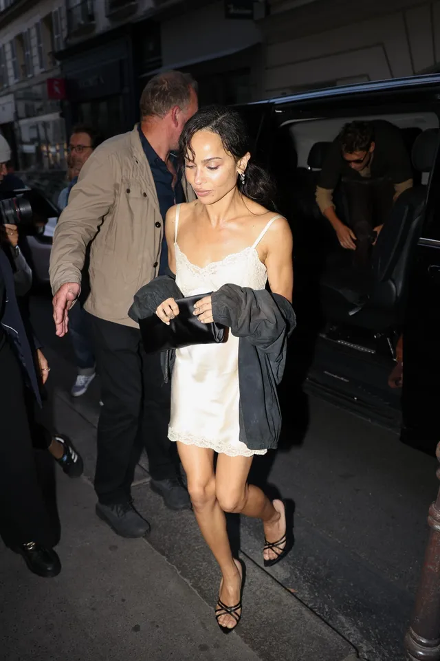 Zoë Kravitz walking beside a car in a short white dress.