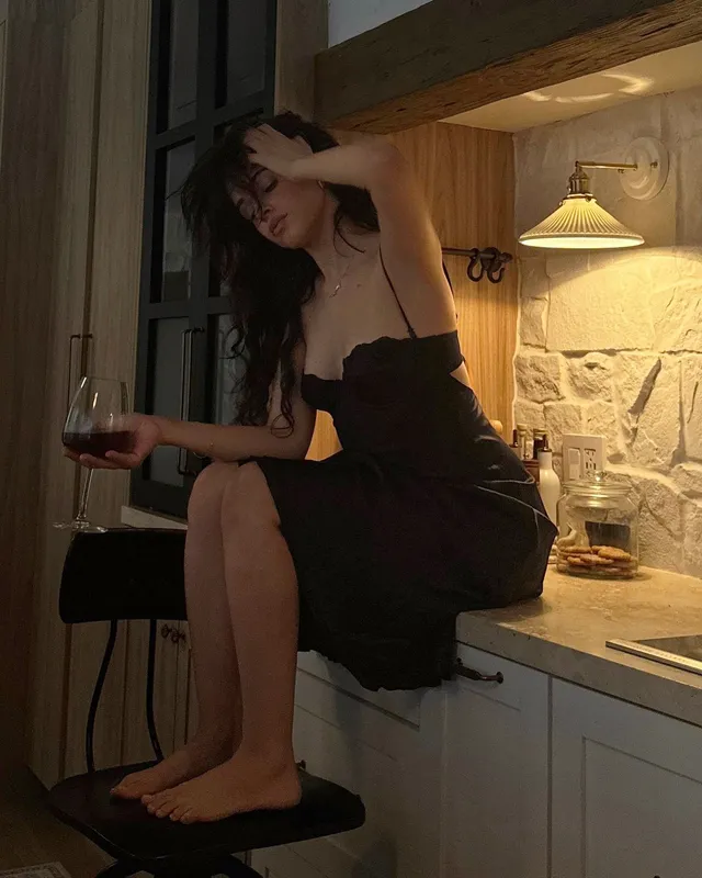 Camila Cabello sitting barefoot on a kitchen counter in a black outfit.
