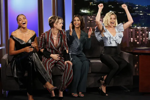 Naomi Scott sitting with guests in a dark suit and heels during a television interview.