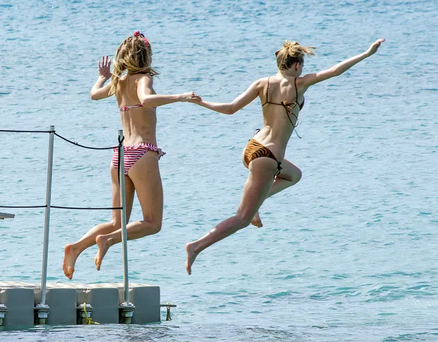 Suki Waterhouse jumping from a dock with a companion.
