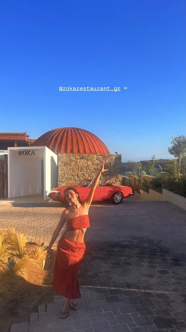 Rachel Zegler posing outdoors in a red outfit beneath a blue sky.